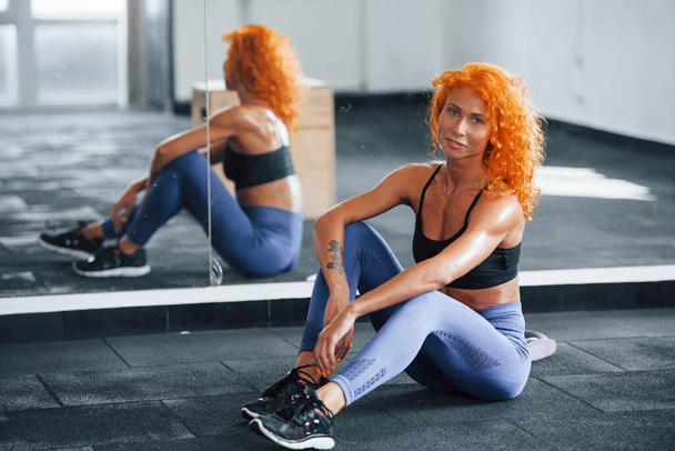 Sitting and taking a break. Sporty redhead girl have fitness day in gym at daytime. Muscular body type. - Fotografie, Obrázek