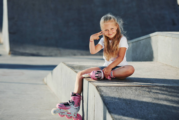 Cute little girl with roller skates outdoors sits on the ramp for extreme sports. - Foto, immagini