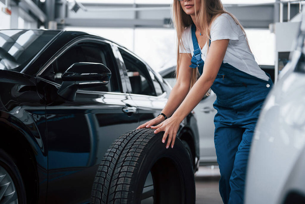 Hurry to make the work as fast as she can. Woman walks with brand new wheel to the car. Conception of repair. - Photo, image