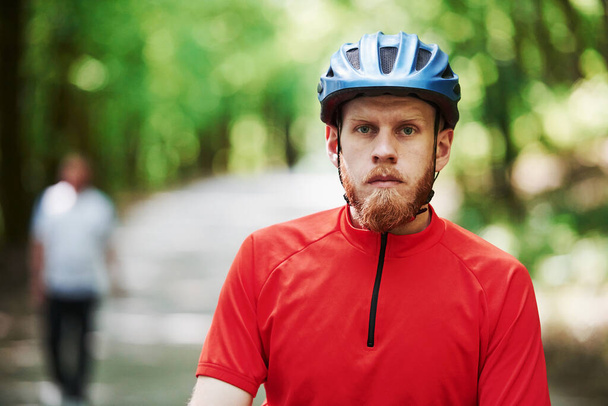 Man in blurred background. Cyclist on a bike is on the asphalt road in the forest at sunny day. - Foto, afbeelding