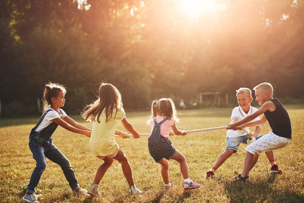 Kids playing tug of war game in the beautiful meadow at sunny day. - Foto, Bild