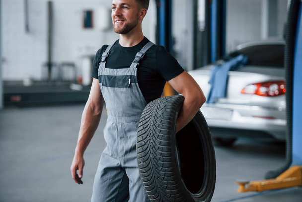 Smiles during the process. Mechanic holds a tire at the repair garage. Replacement of winter and summer tires. - Foto, imagen