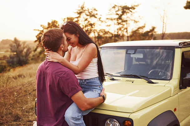 Lovely couple kissing outdoors. Girl sits on green jeep. Beautiful sunny evening. - Photo, Image