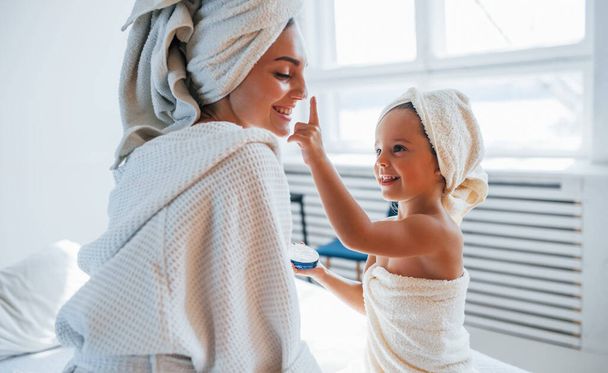 Using cream to clear skin. Young mother with her daugher have beauty day indoors in white room. - Zdjęcie, obraz