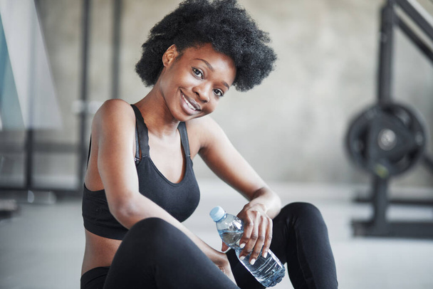 Friendly female taking a break. African american woman with curly hair and in sportive clothes have fitness day in the gym. - Photo, Image