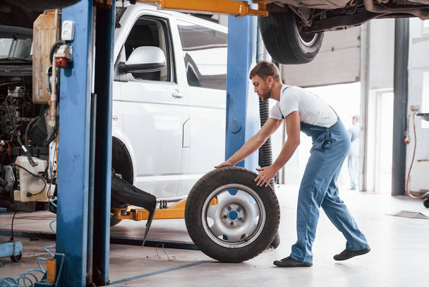 Rolling tire. Employee in the blue colored uniform works in the automobile salon. - Foto, Bild