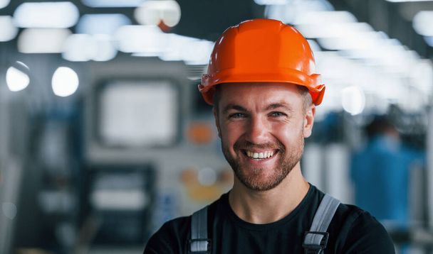 Smiling and happy employee. Portrait of industrial worker indoors in factory. Young technician with orange hard hat. - Fotografie, Obrázek