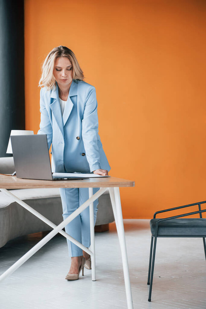 Conception of business. Woman with curly blonde hair indoors in room with orange colored wall and wooden table. - Foto, imagen