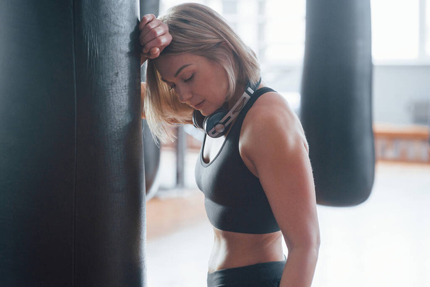 Woman near the black punching bag in the gym. Natural lighting. - Foto, imagen