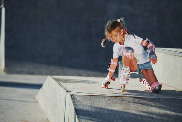 Cute little girl with roller skates outdoors sits on the ramp for extreme sports. - Foto, afbeelding