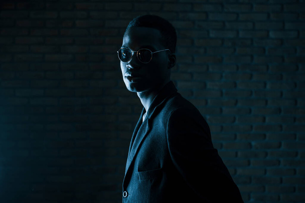 Dark room. Young african american man in the studio. - Фото, изображение