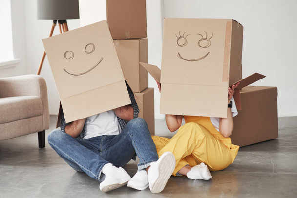 Cute smiles on boxes that is on the heads. Happy couple together in their new house. Conception of moving. - Fotografie, Obrázek