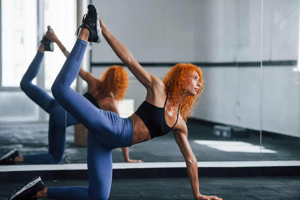 Strength and flexibility. Sporty redhead girl have fitness day in gym at daytime. Muscular body type. - Foto, Imagen