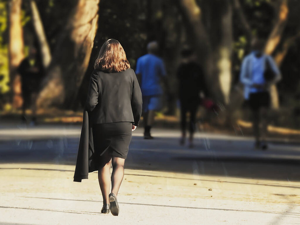 Женщина в черном костюме гуляет по аллее в парке - Фото, изображение