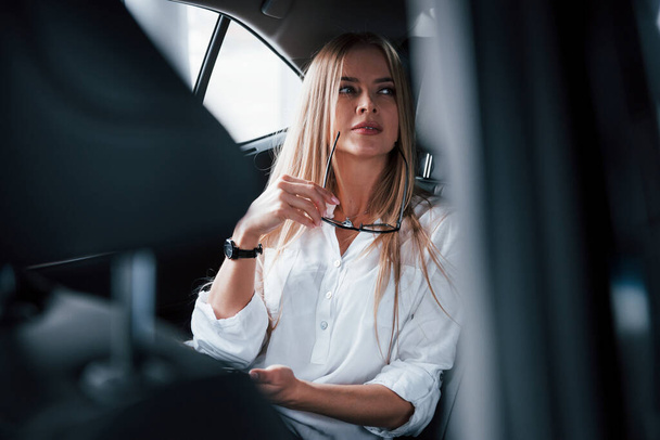 Some deals is coming. Smart businesswoman sits at backseat of the luxury car with black interior. - Foto, Imagen