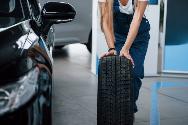 Cropped photo. Woman walks with brand new wheel to the car. Conception of repair. - 写真・画像