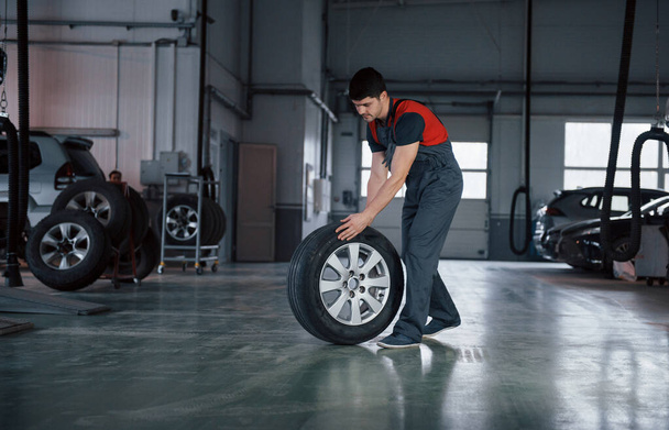 One last wheel. Mechanic holding a tire at the repair garage. Replacement of winter and summer tires. - Zdjęcie, obraz
