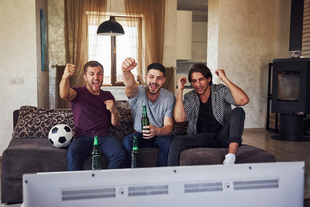 Excited three friends watching soccer on TV at home together. - Foto, Imagen