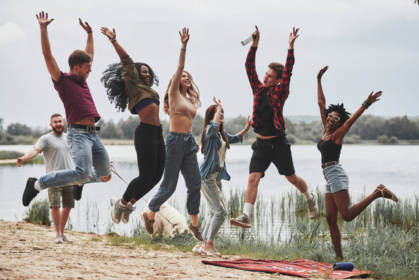 Photo in the air. Everyone is jumping. Group of people have picnic on the beach. Friends have fun at weekend time. - Foto, imagen