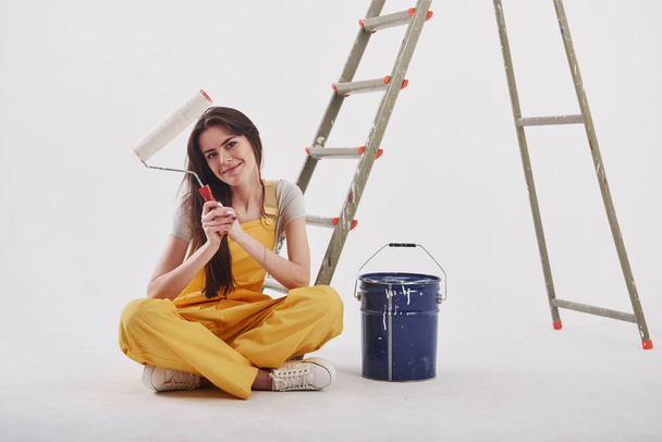 Job well done. Beautiful brunette in yellow uniform and blue colored bucket sits near the ladder. - 写真・画像