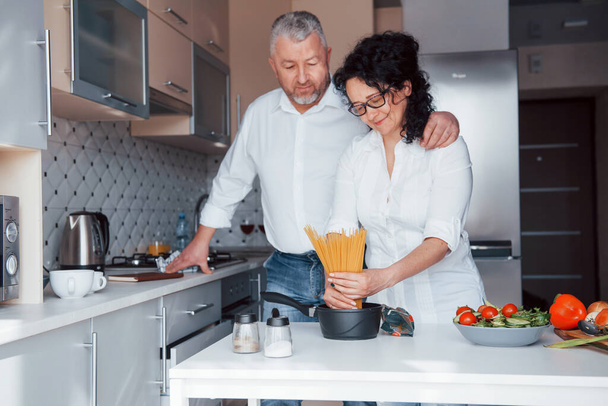 大人は一緒に楽しい時間を過ごす。台所で野菜を使った料理を作る白いシャツを着た男と妻. - 写真・画像