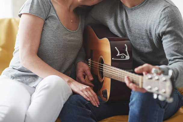 Casual clothes. Playing on acoustic guitar for the girlfriend in the living room of new house. - Foto, imagen