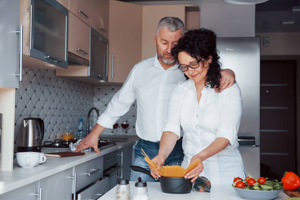 That's my secret recipe. Man and his wife in white shirt preparing food on the kitchen using vegetables. - Foto, afbeelding