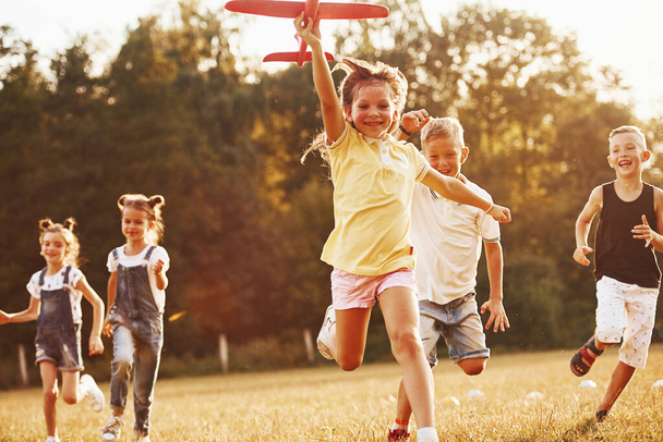 Group of kids having fun outdoors with red toy airplane in hands. - Photo, image