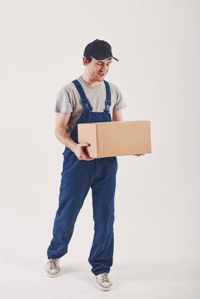 Going to the customer with order. Guy with box in hands stands against white background in the studio. - Zdjęcie, obraz
