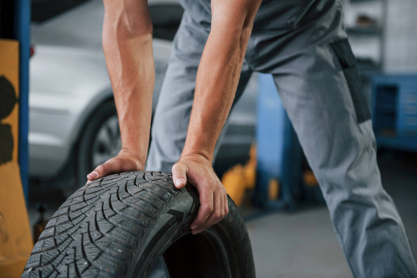 Close up view. Mechanic holds a tire at the repair garage. Replacement of winter and summer tires. - Fotoğraf, Görsel