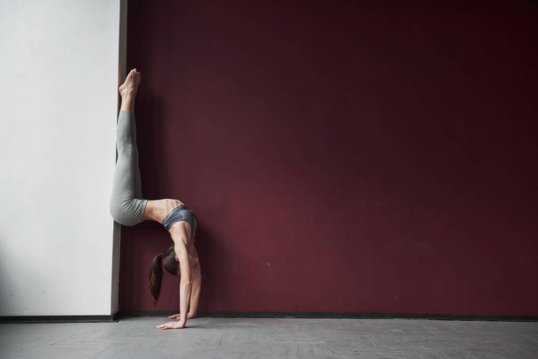 Using wall to make this unbelievable stretch. Girl with good fitness body type have exercises in the spacey room. - Photo, image
