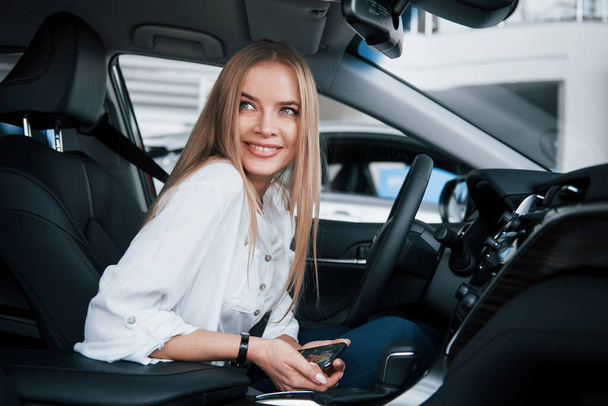 Feeling good. Beautiful blonde girl sitting in the new car with modern black interior. - Photo, Image