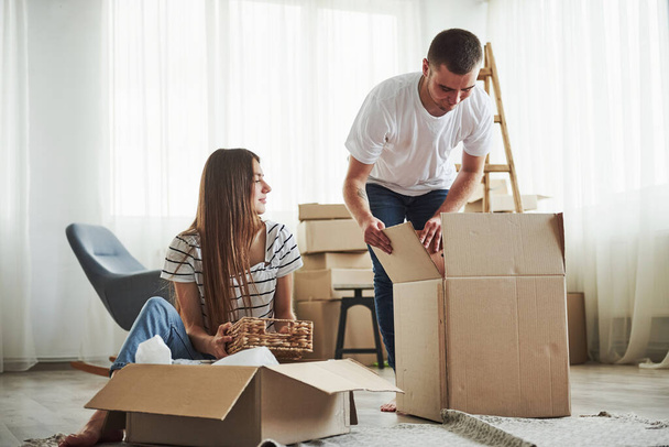 Time to unpack those boxes. Cheerful young couple in their new apartment. Conception of moving. - Фото, изображение