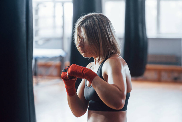 Energy and power. Female boxer is punching the bag. Blonde have exercise in the gym. - Zdjęcie, obraz