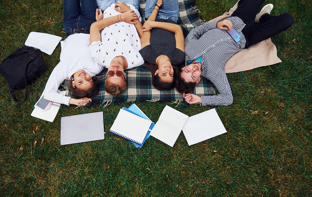 Having good rest. Group of young students in casual clothes on green grass at daytime. - Fotoğraf, Görsel