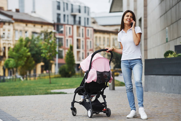 Pretty young mother and her little daughter in pink pram have walk in the city. - Zdjęcie, obraz