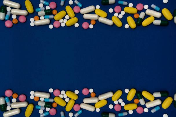 Modré pozadí s kopírovacím prostorem a mnoho léků v kapslích a tabletách různých barev rozptýlených na povrchu - Fotografie, Obrázek