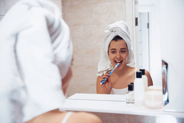 Using toothbrush. In the bathroom. Woman in white towel in head have care of herself. - Foto, Imagem