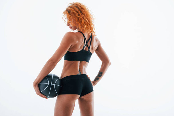 Posing for a camera with soccer ball. Particle view. Redhead female bodybuilder is in the studio on white background. - Foto, Bild