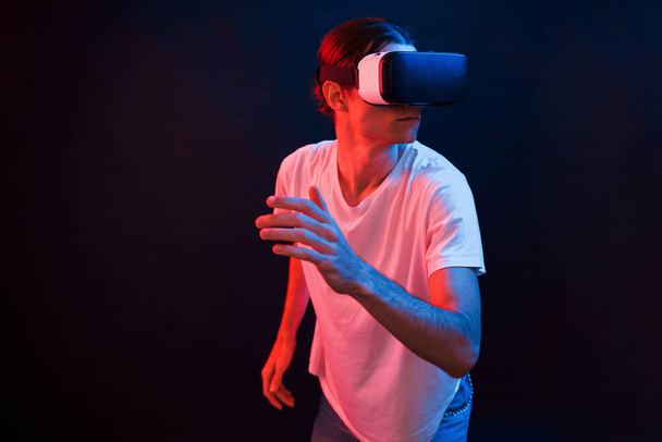 Active leisure. Young man using virtual reality glasses in the dark room with neon lighting. - Foto, Imagem