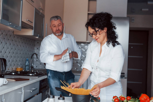 We have dinner. Man and his wife in white shirt preparing food on the kitchen using vegetables. - Φωτογραφία, εικόνα