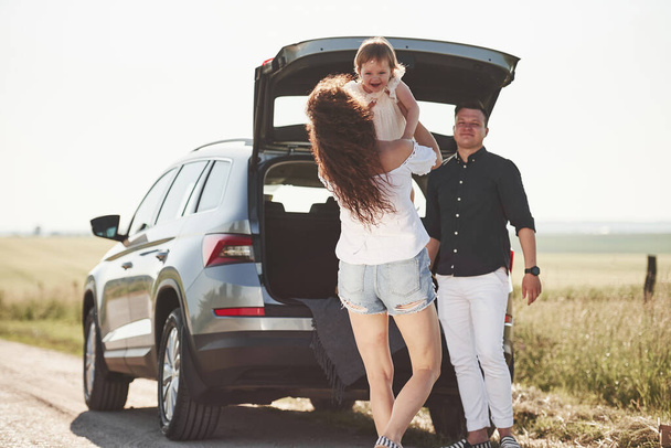 A család jól érzi magát vidéken, az ezüst autó közelében napnyugtakor.. - Fotó, kép
