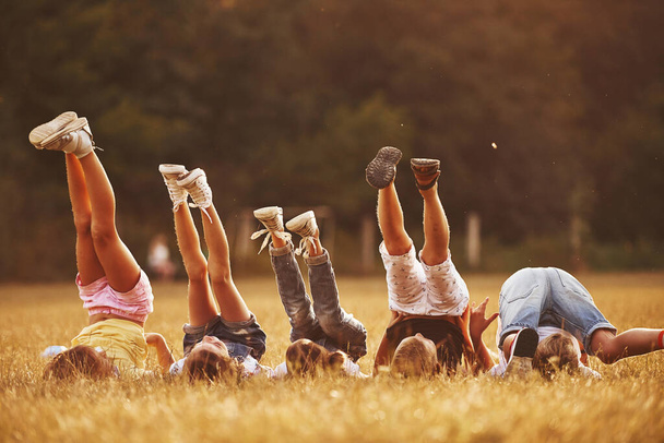 Kids resting in the field at sunny daytime together. Raising legs up. - Фото, изображение