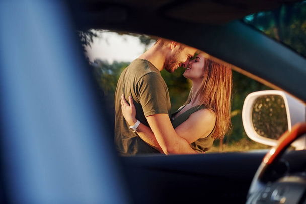 View through the car's window. Beautiful young couple have a good time in the forest at daytime. - Foto, immagini