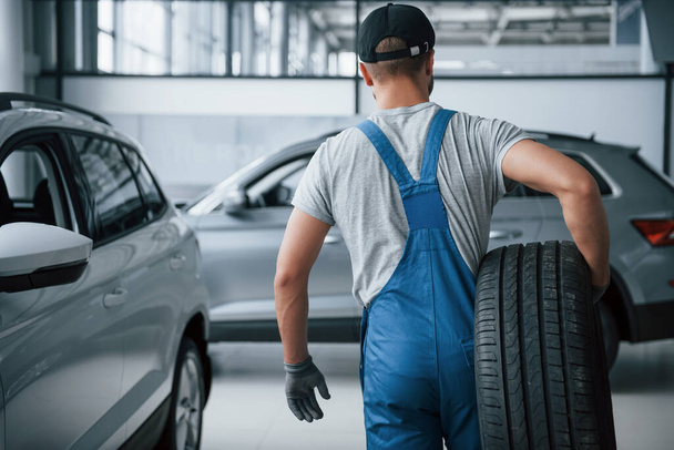This needs to be taken away. Mechanic holding a tire at the repair garage. Replacement of winter and summer tires. - Photo, image