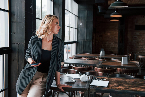 Wireless technologies. Businesswoman with curly blonde hair indoors in cafe at daytime. - Photo, image