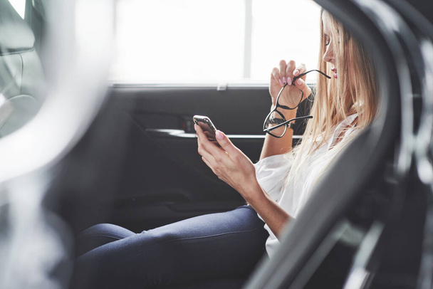 Reading news. Beautiful blonde girl sitting in the new car with modern black interior. - Foto, imagen