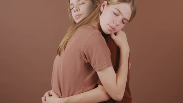 Tilt up shot of young twin sisters embracing against brown background - Footage, Video