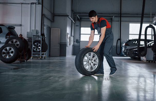 We'll make it quick. Mechanic holding a tire at the repair garage. Replacement of winter and summer tires. - Fotoğraf, Görsel