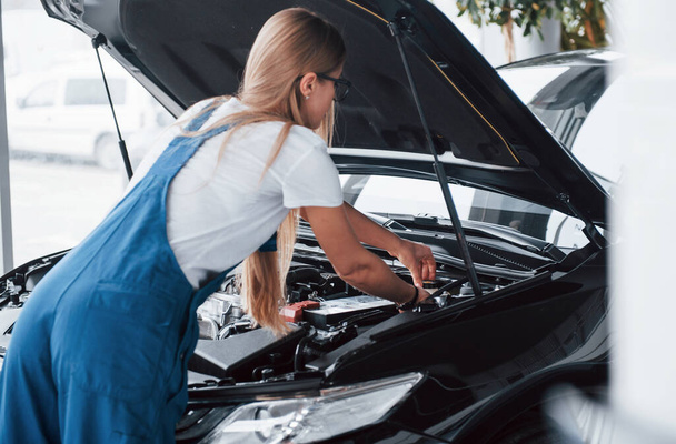 Doing hard work. On the lovely job. Car addicted woman repairs black automobile indoors. - Photo, image